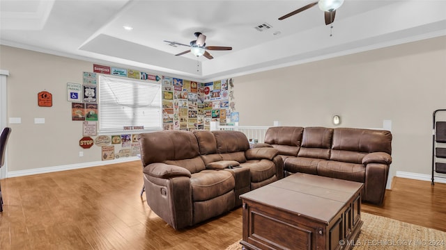 living room featuring ceiling fan, a raised ceiling, ornamental molding, and light hardwood / wood-style flooring