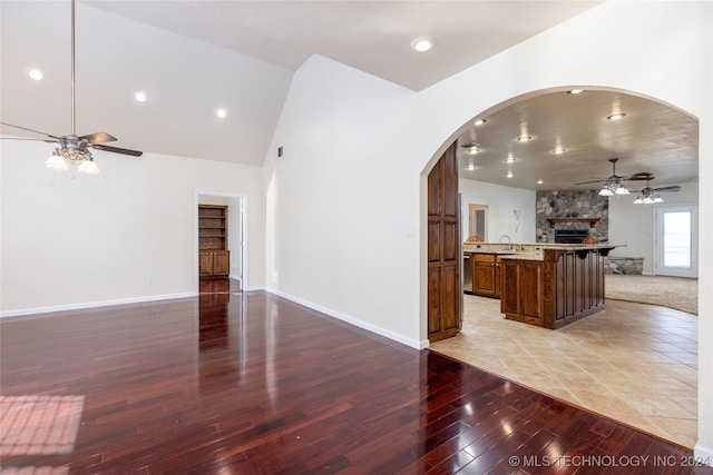 unfurnished living room with a ceiling fan, light wood finished floors, a stone fireplace, arched walkways, and recessed lighting