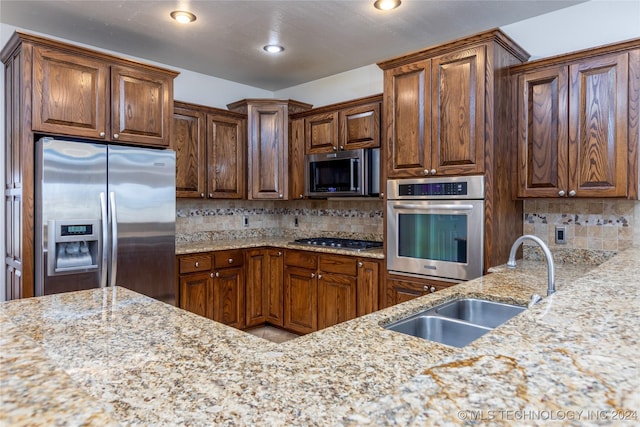 kitchen with appliances with stainless steel finishes, a sink, tasteful backsplash, and light stone countertops