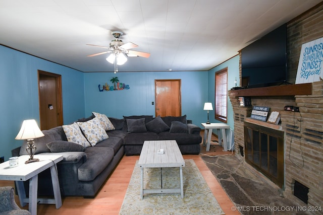 living room with a stone fireplace, wood-type flooring, and ceiling fan