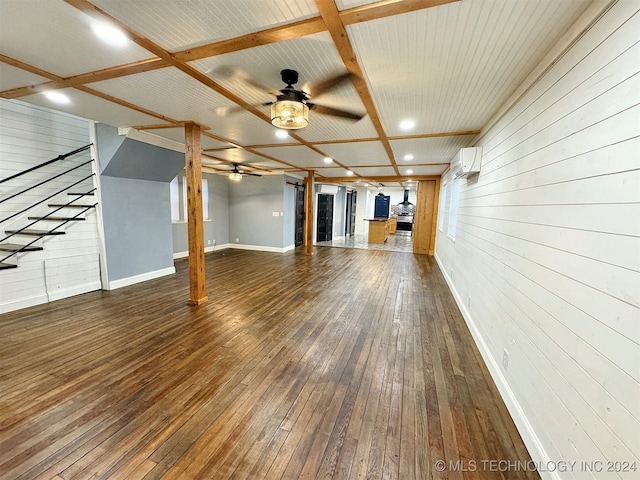 unfurnished living room featuring wood walls, beamed ceiling, a wall mounted air conditioner, ceiling fan, and dark hardwood / wood-style flooring