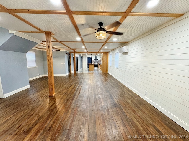 unfurnished living room featuring a wall mounted AC, wood walls, dark wood-type flooring, beamed ceiling, and ceiling fan