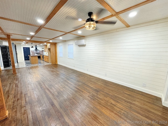 unfurnished living room featuring wood walls, a wall unit AC, ceiling fan, beam ceiling, and wood-type flooring