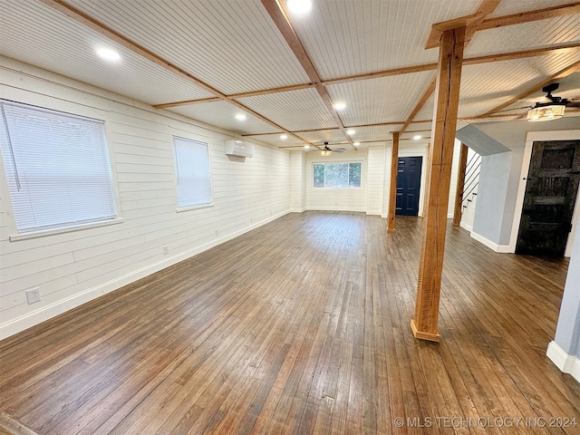 unfurnished living room with an AC wall unit, dark wood-type flooring, ceiling fan, and wooden walls