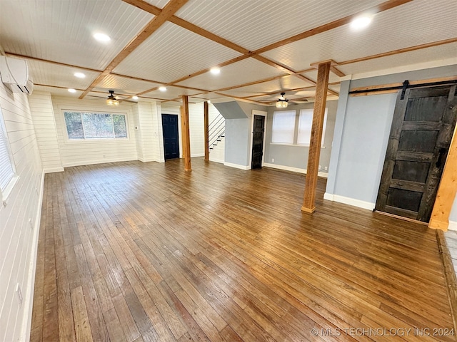 unfurnished living room featuring an AC wall unit, a barn door, dark hardwood / wood-style floors, and wooden ceiling