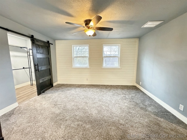 carpeted spare room featuring a textured ceiling, wood walls, a barn door, and ceiling fan