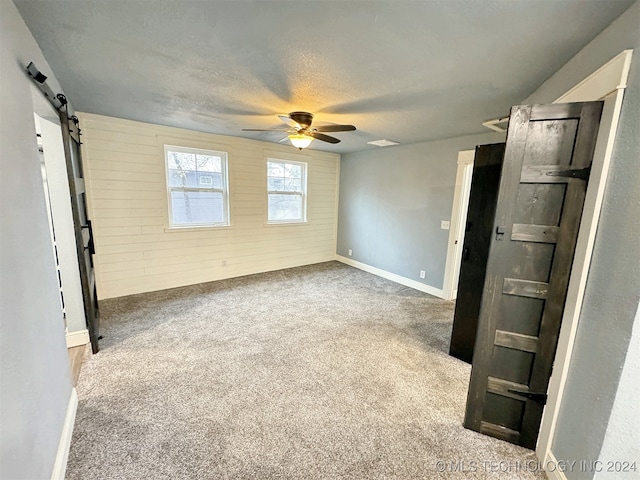 unfurnished room featuring carpet floors, a textured ceiling, a barn door, wooden walls, and ceiling fan