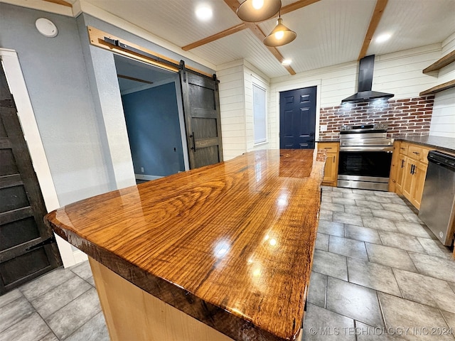 kitchen with butcher block countertops, stainless steel appliances, a barn door, beamed ceiling, and wall chimney exhaust hood