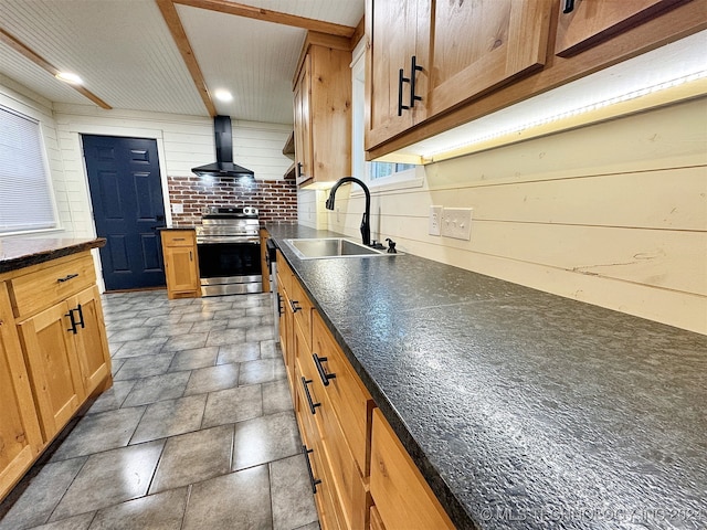 kitchen with wall chimney range hood, stainless steel stove, wood walls, decorative backsplash, and sink