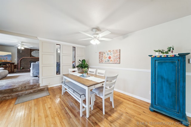 dining area featuring light wood-type flooring, a fireplace, and ceiling fan