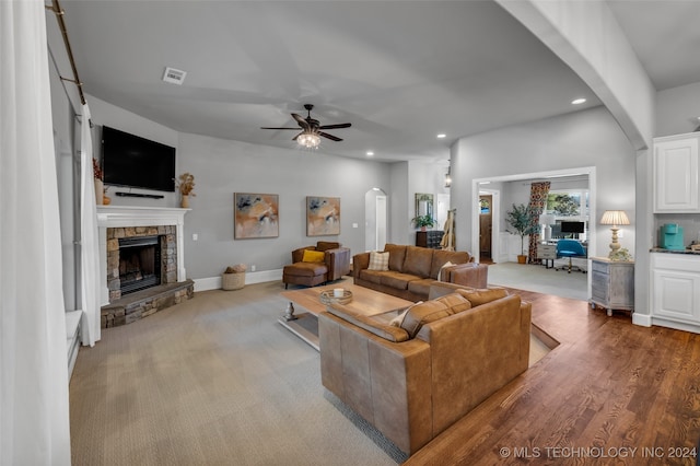 living room featuring ceiling fan, light hardwood / wood-style flooring, and a stone fireplace