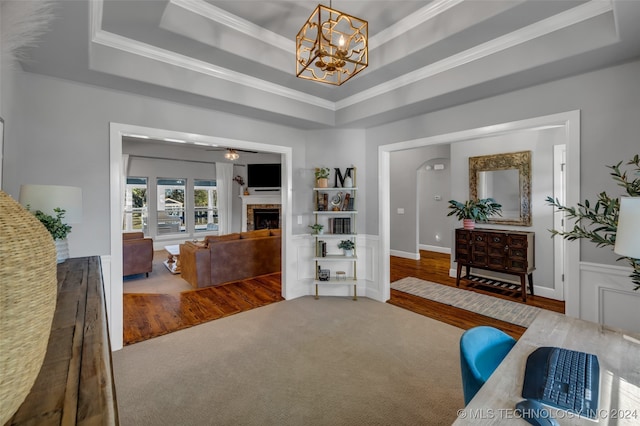 living area with a raised ceiling, an inviting chandelier, ornamental molding, and hardwood / wood-style flooring