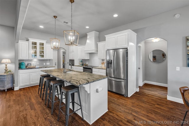 kitchen featuring appliances with stainless steel finishes, an island with sink, white cabinetry, and custom range hood