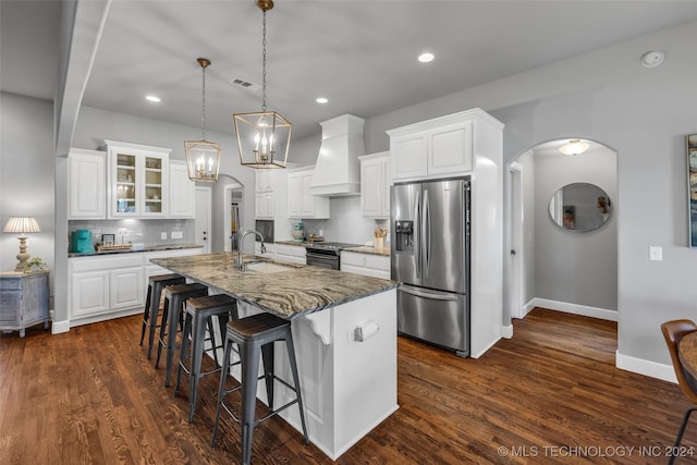 kitchen featuring stainless steel appliances, arched walkways, custom exhaust hood, a sink, and tasteful backsplash