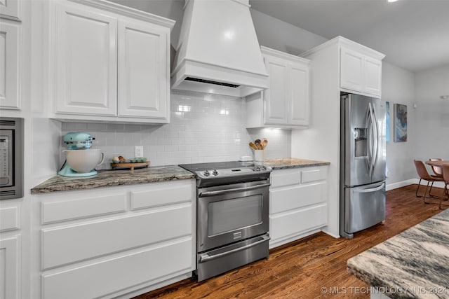 kitchen featuring white cabinets, stainless steel appliances, dark stone countertops, and premium range hood