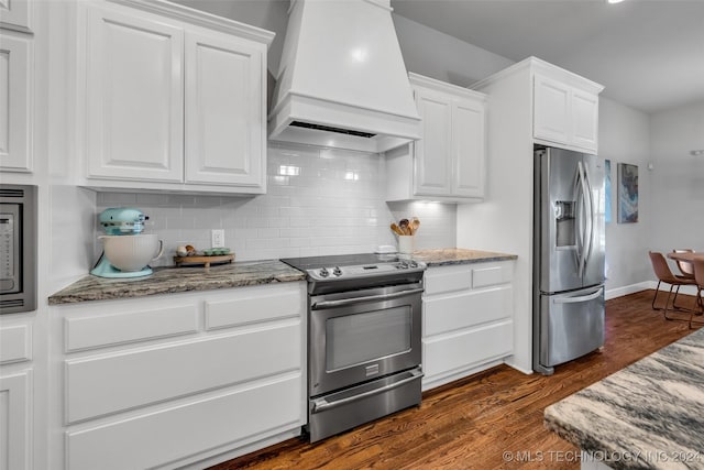 kitchen featuring stainless steel appliances, premium range hood, dark wood finished floors, white cabinetry, and decorative backsplash