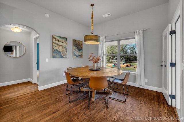 dining space featuring wood finished floors, baseboards, and arched walkways