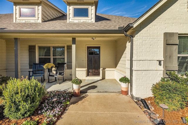 entrance to property featuring a porch, brick siding, and a shingled roof
