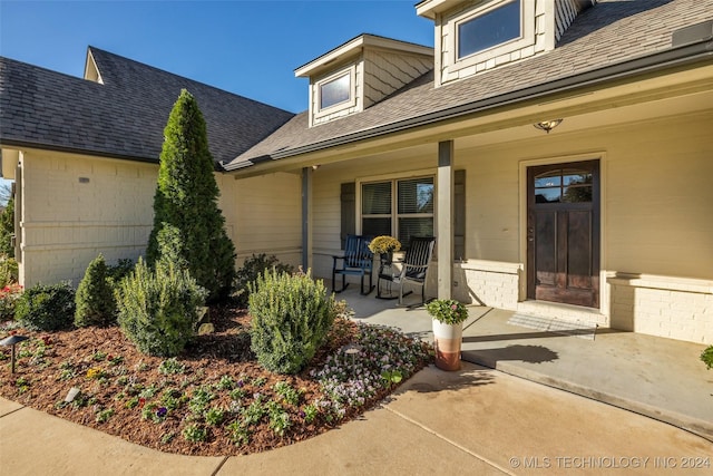 entrance to property with a porch and roof with shingles