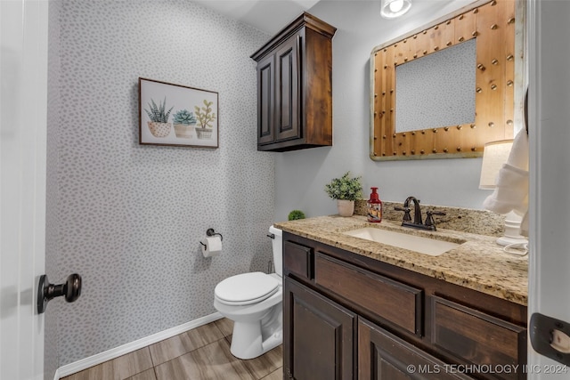 half bath with baseboards, toilet, wallpapered walls, vanity, and wood finished floors