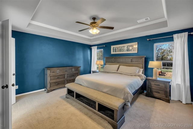 bedroom with a tray ceiling, light colored carpet, baseboards, and ceiling fan