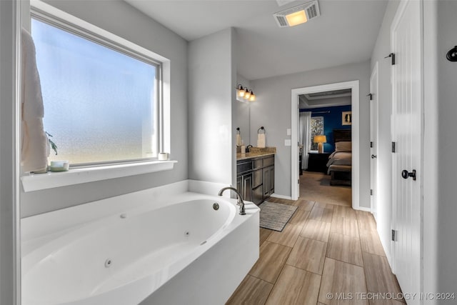 ensuite bathroom with a jetted tub, vanity, wood tiled floors, and baseboards