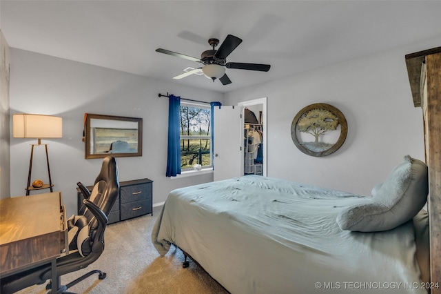 bedroom with light carpet, an office area, a ceiling fan, a walk in closet, and baseboards