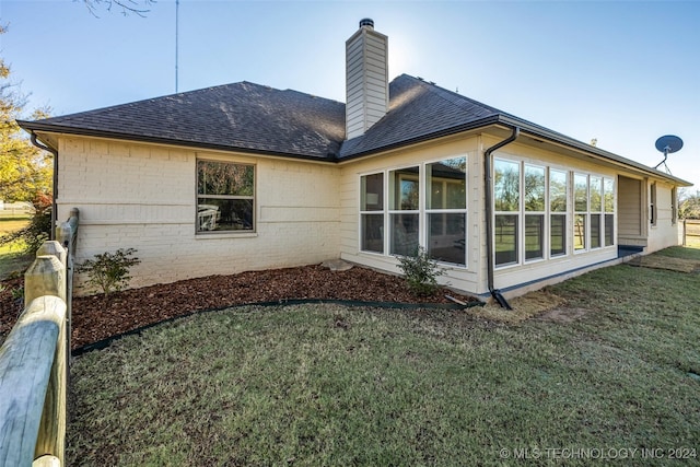 back of house with a shingled roof, a sunroom, brick siding, and a chimney