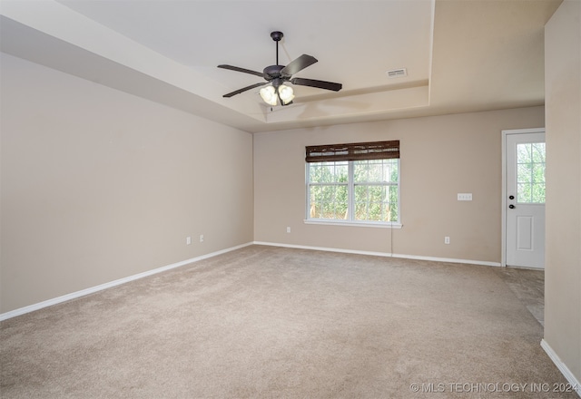 spare room with ceiling fan, a tray ceiling, and carpet