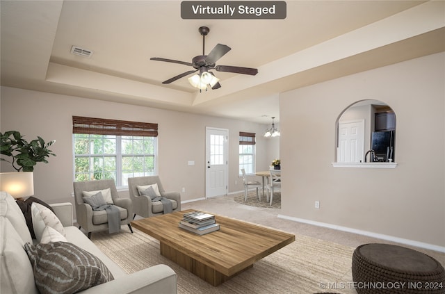 carpeted living room featuring ceiling fan with notable chandelier and a raised ceiling