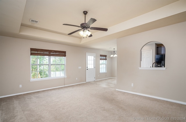 carpeted empty room with ceiling fan with notable chandelier and a tray ceiling