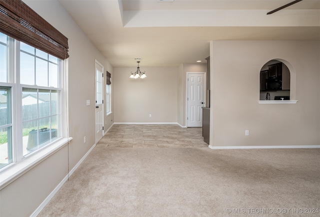 spare room featuring a wealth of natural light, a chandelier, and light carpet