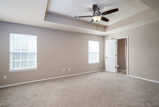 carpeted empty room featuring ceiling fan and a raised ceiling