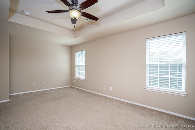 carpeted empty room with plenty of natural light, ceiling fan, and a raised ceiling