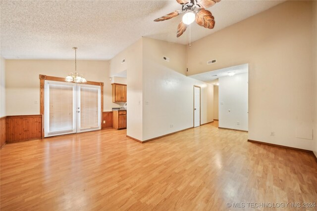 unfurnished living room featuring ceiling fan with notable chandelier, a textured ceiling, light hardwood / wood-style flooring, and high vaulted ceiling