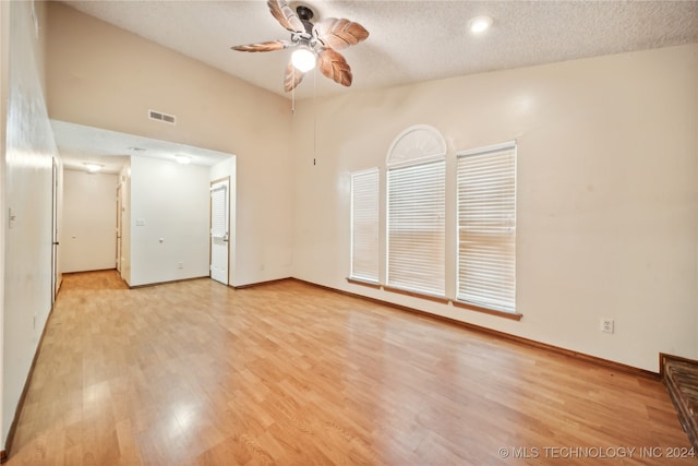 spare room with a towering ceiling, a textured ceiling, ceiling fan, and light hardwood / wood-style flooring