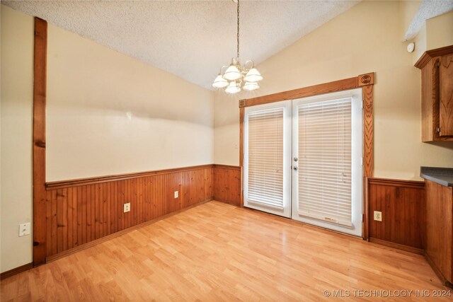 unfurnished dining area with light wood-type flooring, a notable chandelier, a textured ceiling, and vaulted ceiling