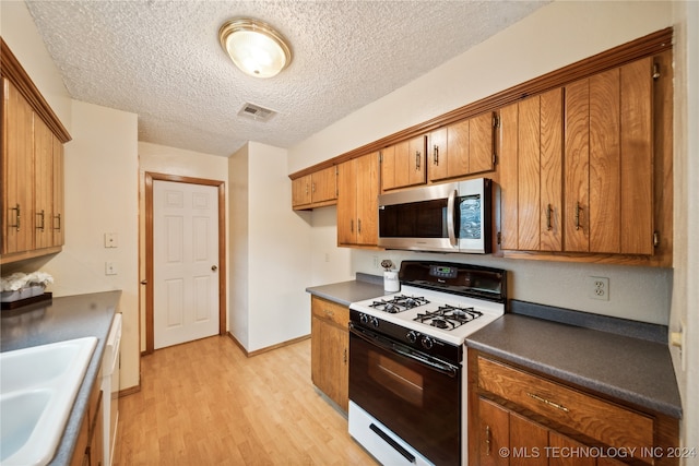 kitchen with light wood-type flooring, a textured ceiling, white appliances, and sink