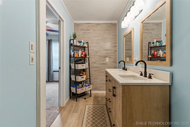 bathroom with vanity, wooden walls, hardwood / wood-style flooring, ornamental molding, and a textured ceiling