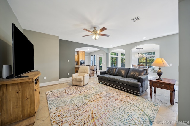 tiled living room with ceiling fan with notable chandelier