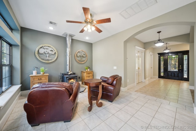 living room featuring a wood stove, ceiling fan, and light tile patterned floors