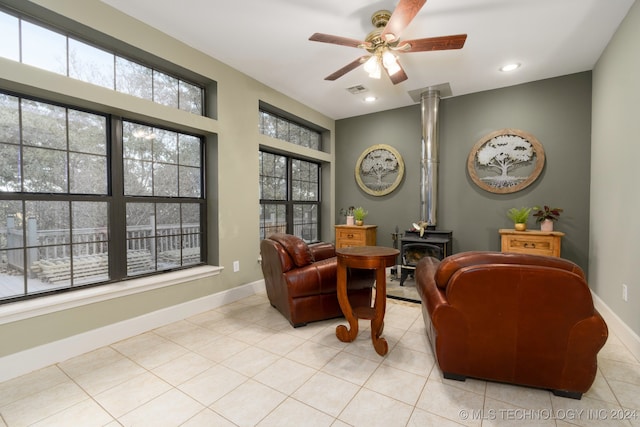 living area with ceiling fan, light tile patterned flooring, a wood stove, and ornate columns