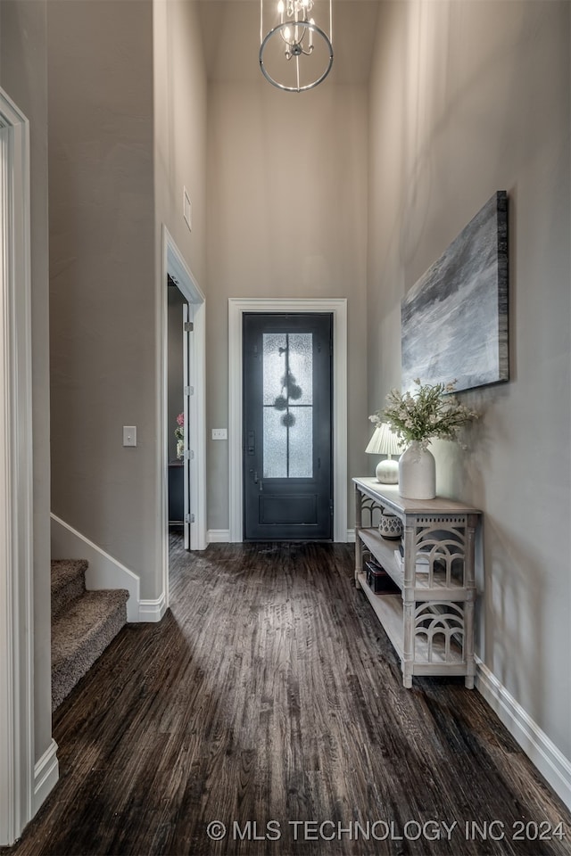 entryway with a towering ceiling, dark wood-type flooring, and a chandelier