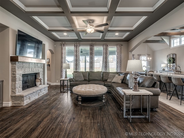 living room featuring dark hardwood / wood-style floors, a healthy amount of sunlight, a stone fireplace, and beam ceiling