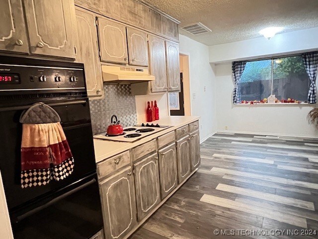 kitchen featuring dark wood-type flooring, black oven, white cooktop, a textured ceiling, and decorative backsplash