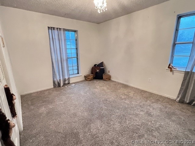 carpeted spare room featuring a chandelier and a textured ceiling