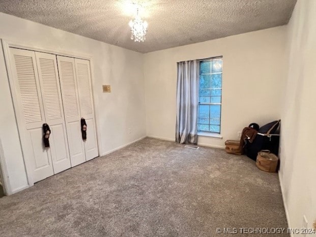 unfurnished bedroom featuring a notable chandelier, a closet, a textured ceiling, and carpet flooring