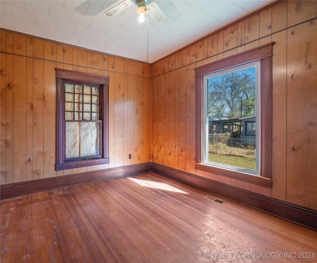 empty room with wooden walls, hardwood / wood-style floors, and ceiling fan