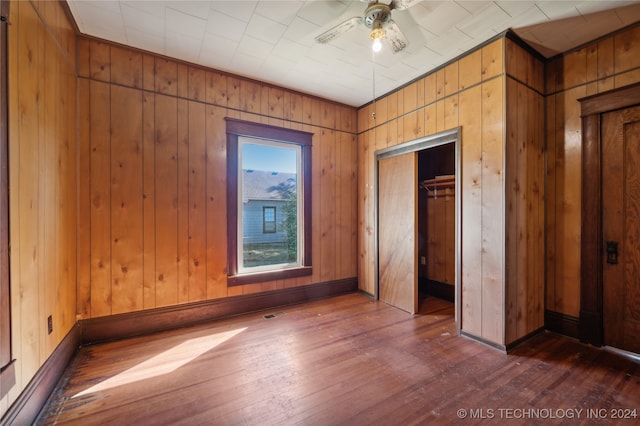 unfurnished bedroom featuring wood walls, dark wood-type flooring, ceiling fan, and a closet