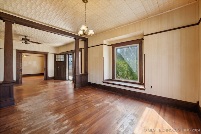 interior space featuring dark wood-type flooring, wood walls, decorative columns, and ceiling fan with notable chandelier